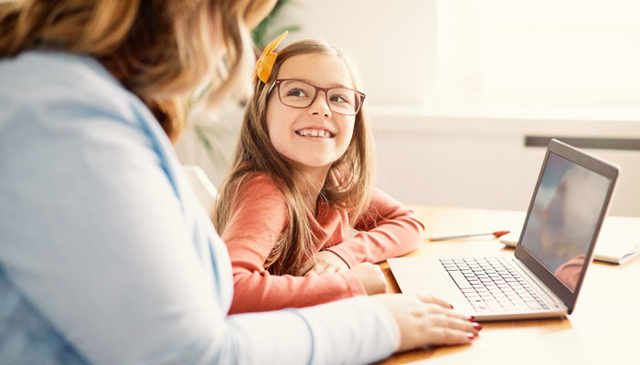 a young girl smiles as she uses her computer with her mother